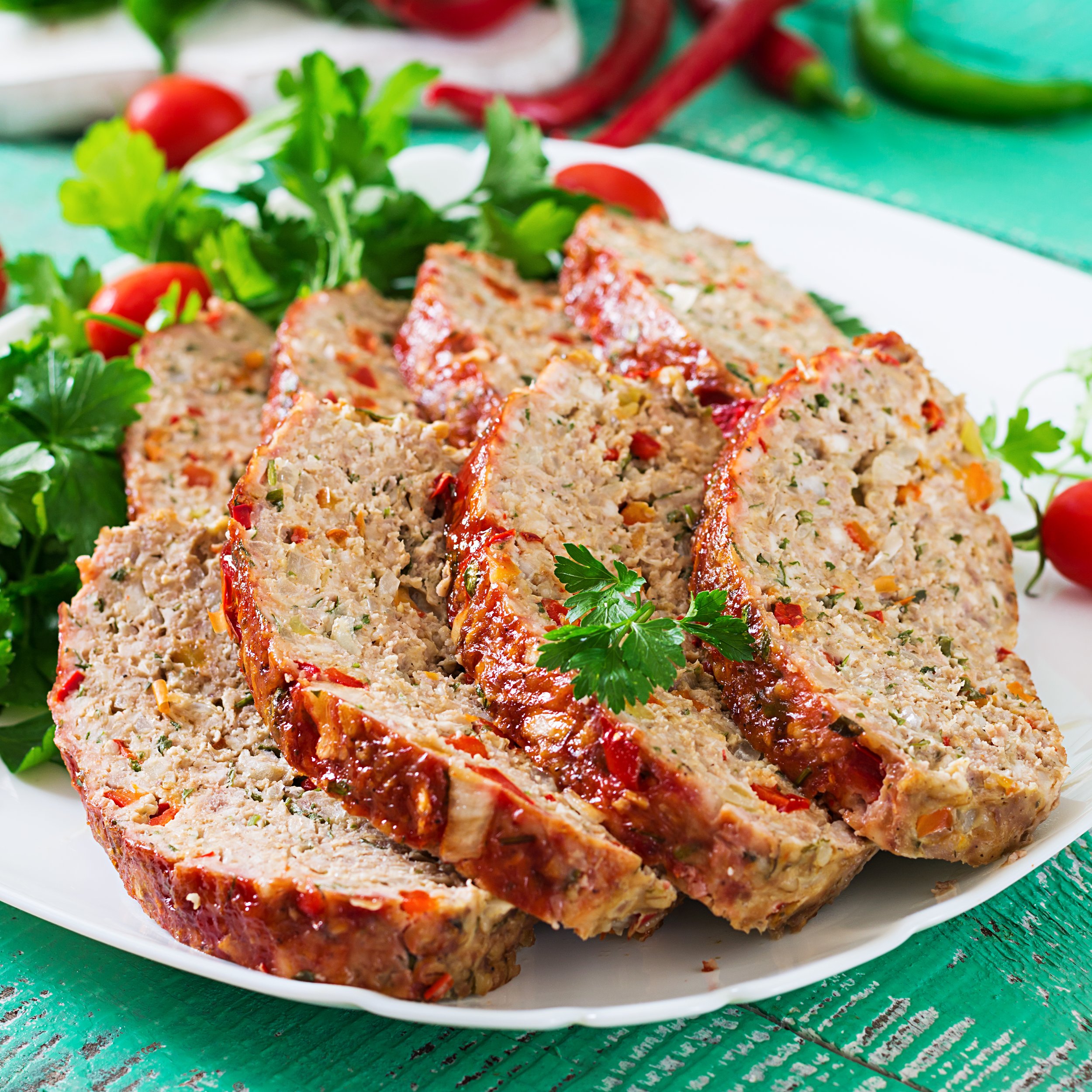 Sliced meatloaf served on a white platter, garnished with fresh parsley and cherry tomatoes, showcasing a delicious homemade dish with colorful ingredients.